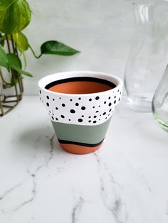 a white and green cup sitting on top of a table next to a glass vase