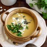 a white plate topped with a bowl of soup and garnished with parsley