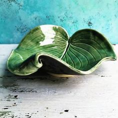 a green leaf shaped bowl sitting on top of a wooden table next to a blue wall