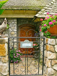 an iron gate in front of a stone house with potted plants and flowers around it