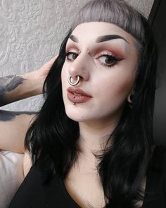 a woman with black hair and piercings on her nose is posing for the camera