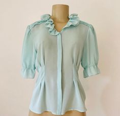 "Vintage 1960s feminine aqua top from Helena International, featuring exquisite retro detailing such as a ruffled collar, gentle pleating at the shoulders, front and back tucks for fabulous fit, and gathered sleeves ending at the elbow in ruffles. Hidden front button placket. Semi transparent. 100% polyester. Approximate Measurements: Chest: 36\"; Waist: Up to 29\"; Length: 22\" Labeled a size 6 Retro beauty, circa 1960s, is in excellent vintage condition, with no indication it was ever even wor Peach Skirt, Back Tuck, Retro Beauty, Feminine Top, Gathered Sleeves, Ruffled Collar, Semi Transparent, Green Blouse, Vintage 1960s