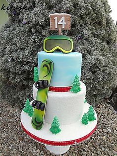 a snowboarder themed birthday cake is displayed in front of a tree and bushes