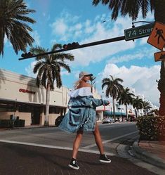 a woman walking across a street under a traffic light with palm trees in the background