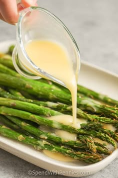 asparagus being drizzled with dressing on a white platter, ready to be eaten