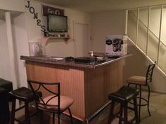 a small bar with three stools and a television on the wall behind it in a living room