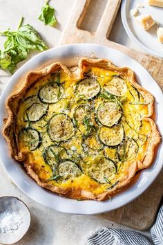 a quiche with zucchini and cheese on a white plate next to other dishes