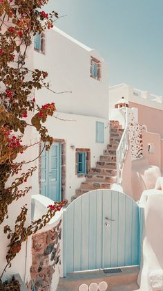 a white building with blue doors and steps leading up to the door is surrounded by pink flowers