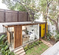 a small house with a yellow door and some plants on the side of the building