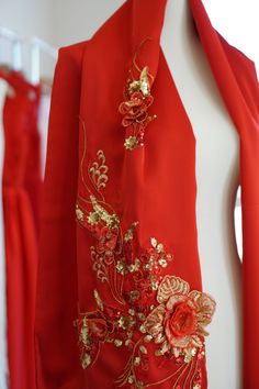 a red dress with gold embroidered flowers on it and a jacket hanging from the wall