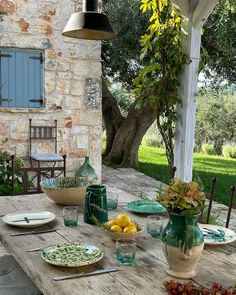 a wooden table topped with plates and bowls next to a stone wall covered in greenery