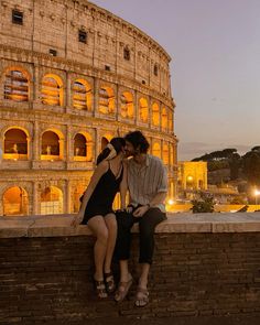 two people are sitting on a wall in front of the colossion at night