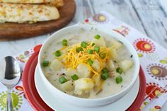 a bowl of potato soup with cheese and green onions on a red plate next to some crackers