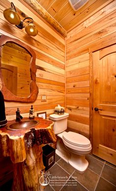 a bathroom with wooden walls and flooring, including a sink, toilet and mirror