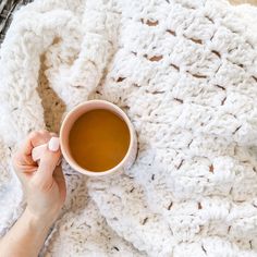 a person holding a cup of coffee on top of a white crocheted blanket