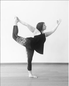 a woman in black shirt doing a yoga pose on wooden floor with white wall behind her