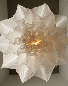 a large white flower hanging from the ceiling in front of a light fixture that is lit up