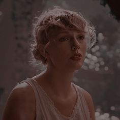 a woman with blonde hair wearing a white top and looking off to the side in front of a fountain