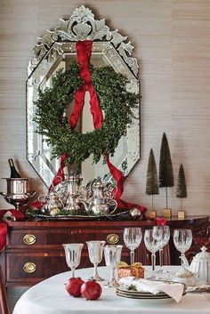 a dining room table with wine glasses and a wreath on the wall above it, surrounded by christmas decorations