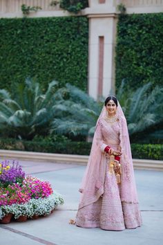 a woman in a pink bridal gown standing next to some flowers and greenery