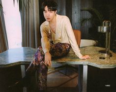 a young man sitting on top of a marble desk next to a plant and lamp