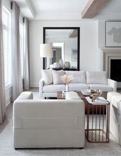 a living room filled with white furniture next to a fire place and a mirror on the wall