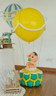 a baby in a hot air balloon floating on top of a wooden floor next to a cake