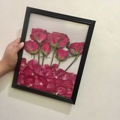 a person holding up a frame with pink flowers in it