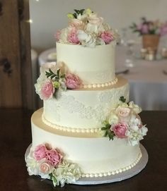 a three tiered wedding cake with pink and white flowers on the top, sitting on a table