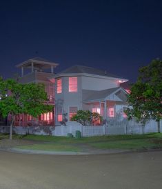 a large white house with red lights on it's windows in the night time