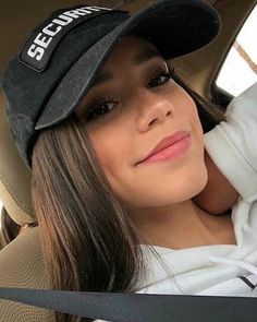 a woman sitting in the back seat of a car wearing a black hat and white shirt