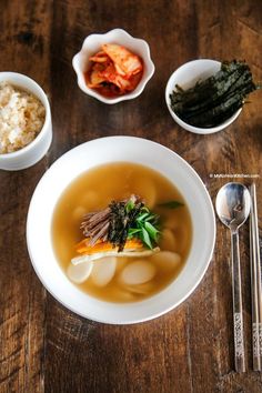 a bowl filled with soup next to bowls of rice and other foods on a wooden table