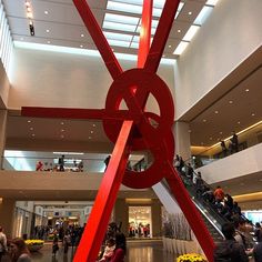 a large red sculpture in the middle of a building with people walking around it and onlookers