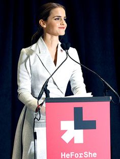 a woman standing at a podium with a microphone in her hand and wearing a white coat