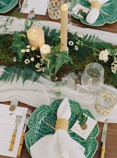 the table is set with green and white plates, silverware, candles, and greenery