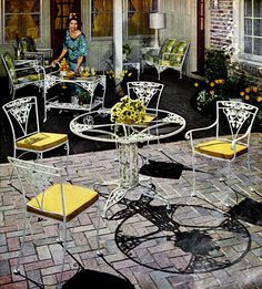 the woman is sitting on the patio with yellow chairs and white tables in front of her