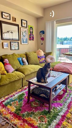 a cat sitting on top of a coffee table in front of a couch with colorful pillows