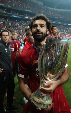 a man holding a trophy in front of his face on a soccer field with other people