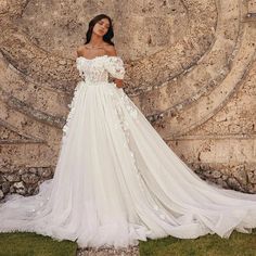 a woman standing in front of a stone wall wearing a wedding dress with flowers on it