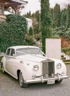 an old white car is parked in front of a building with greenery on it