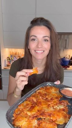 a woman holding up a piece of pizza in front of her face and smiling at the camera