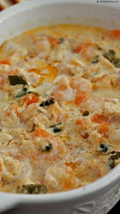 a white casserole dish filled with chicken and vegetable soup on top of a wooden table