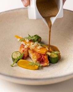 someone is pouring sauce on some food in a white bowl with cucumbers and peppers