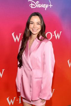 a woman in a pink suit posing for a photo on the disney world red carpet