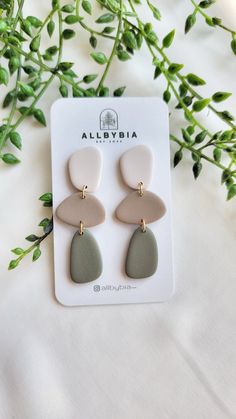 the grey and white earrings are on display next to some green plant leaves in front of it