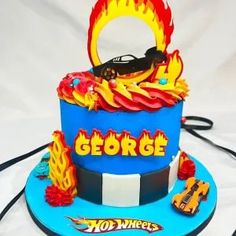 a blue cake with flames on it and the word george written in large letters, surrounded by other decorations