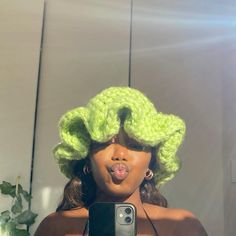 a woman taking a selfie in front of a mirror wearing a green crochet wig