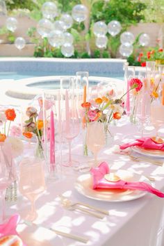 the table is set with pink and orange flowers in vases, plates and utensils