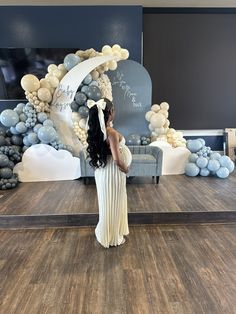 a woman in a white dress standing on a stage with balloons and decorations behind her