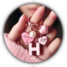 a hand holding a pink key chain with hearts on it and a letter h in the middle